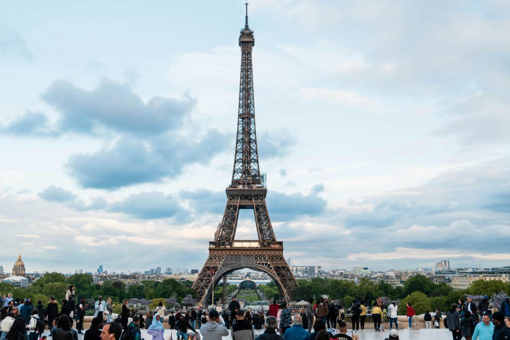 Iconic view of the Eiffel Tower in Paris surrounded by tourists on a cloudy day.